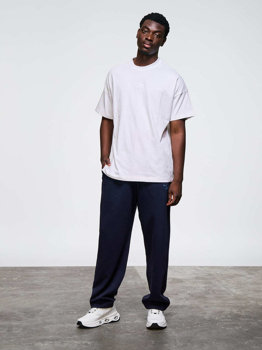 Un homme de face porte un t-shirt blanc modèle fabricio, un pantalon de jogging noir et des sneakers Namib Airness blanc &amp; noir