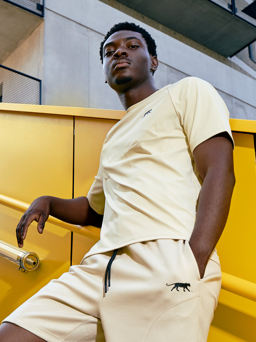 T-shirt Oslo en écru porté par un homme en tenue de sport Airness accoudée à la rampe d'un escalier 