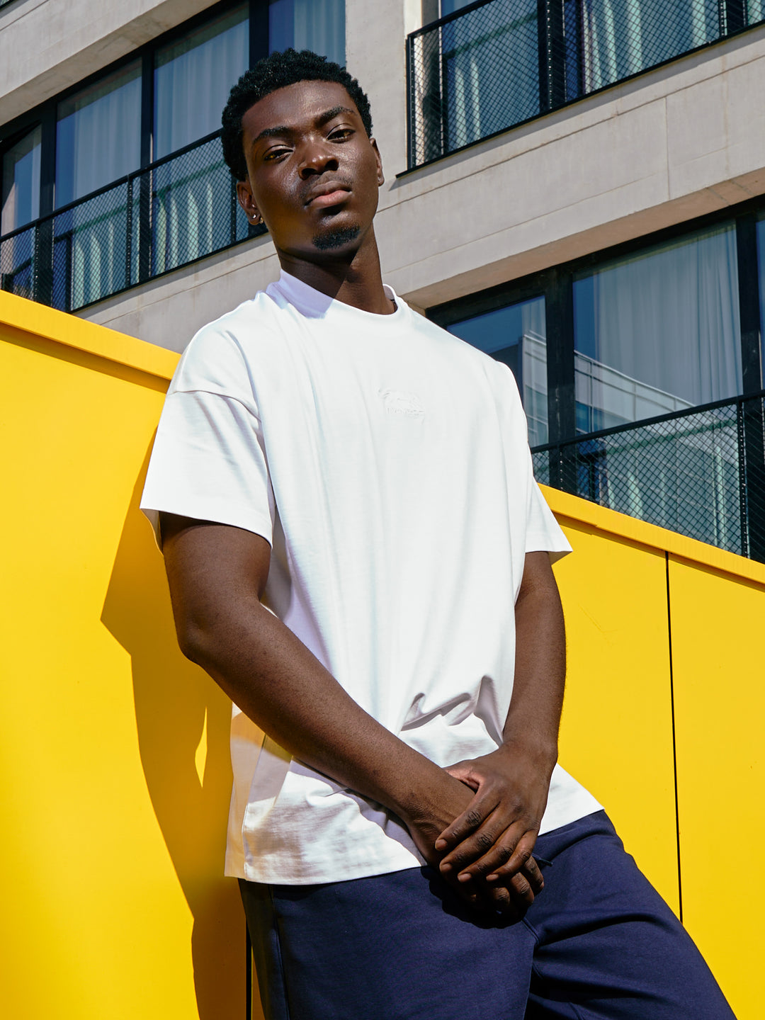 t-shirt Fabricio Airness blanc porté par un homme adossé à un mur jaune